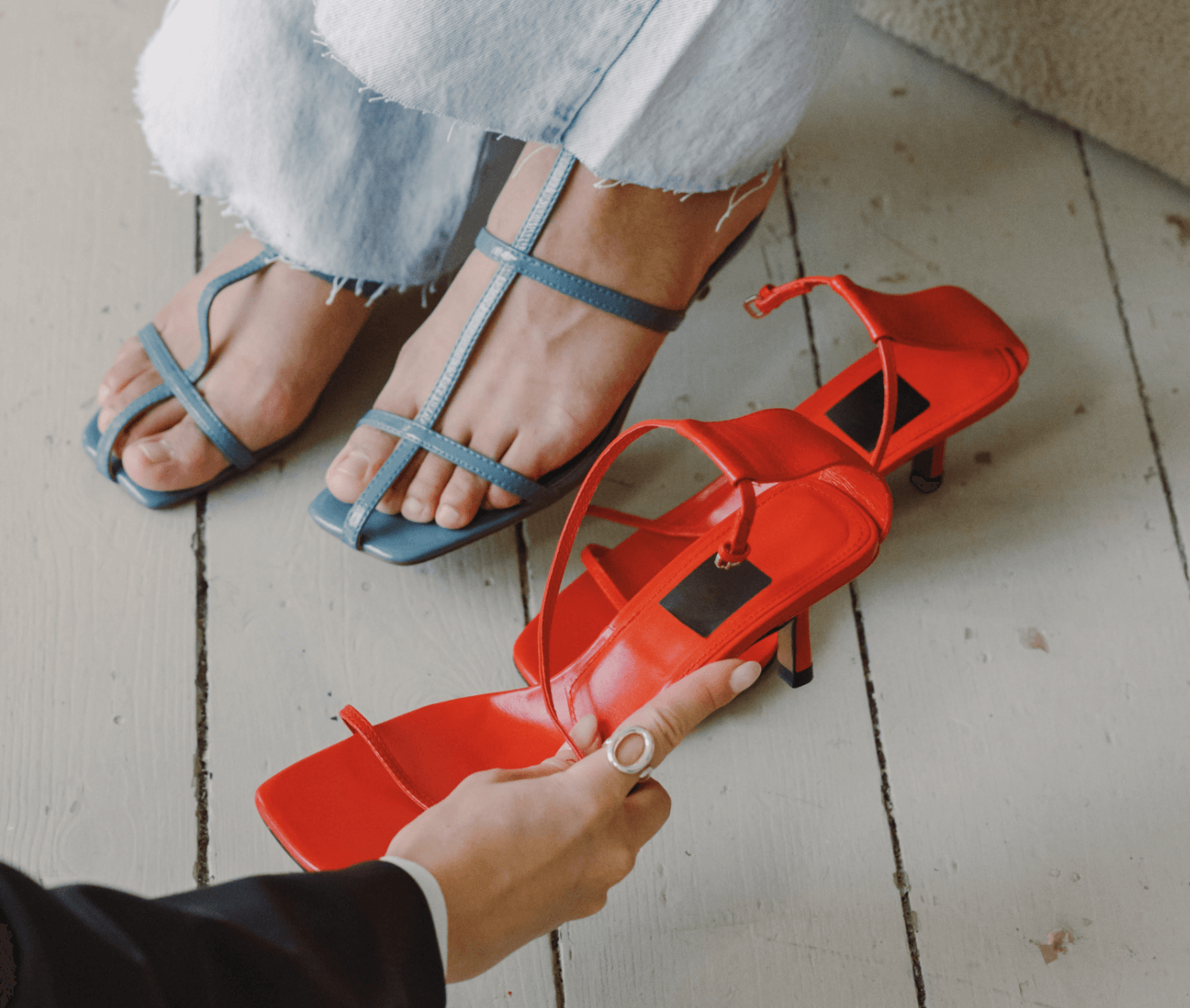 Siniset sandaletit naisen jalassa ja punaiset sandaletit lattialla