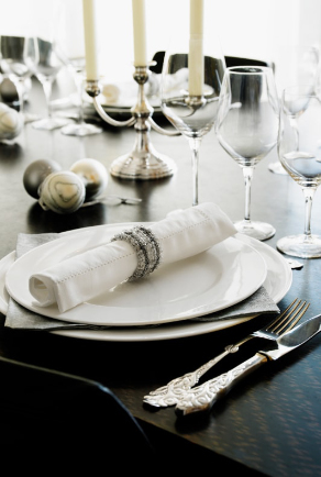 Joulupöytä joka on katettu klassisesti valkoisin tekstiilein ja koristeltu kultaisin ja hopeaisin joulukuusenkoristein
