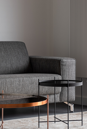 Tummanharmaa sohva sekä yksinkertaiset metalliset sohvapöydät